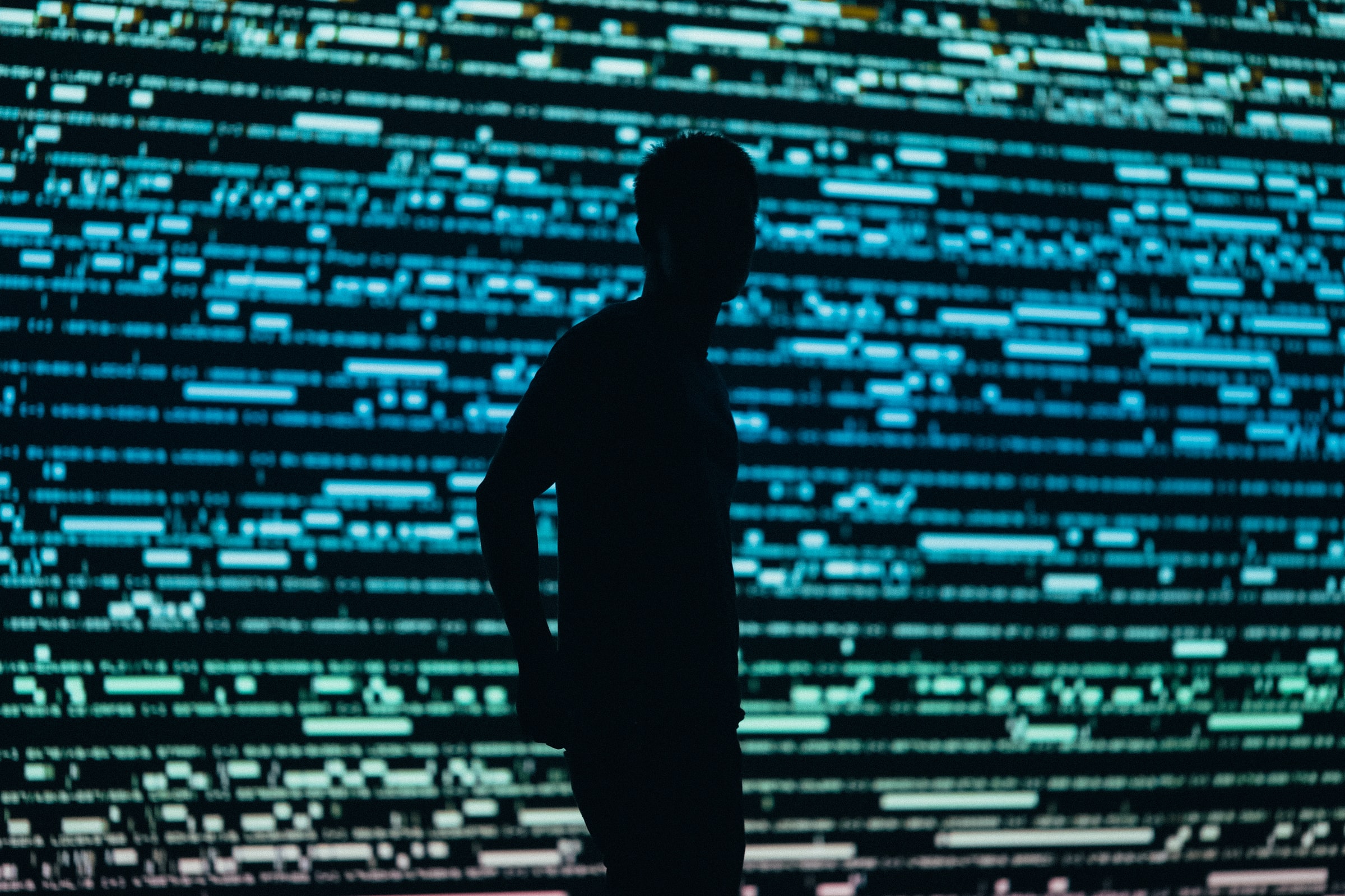 Photo of a silhouette of a man against a large screen showing computer data